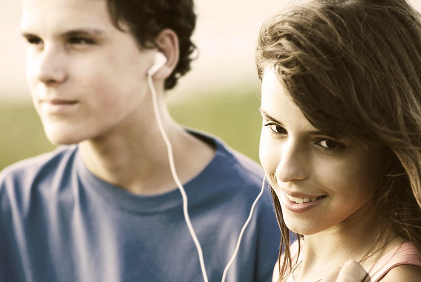 Teens sharing earphones, listening music outdoor. Summer time. Image is captured in 12 bit RAW and processed in Adobe RGB color space.