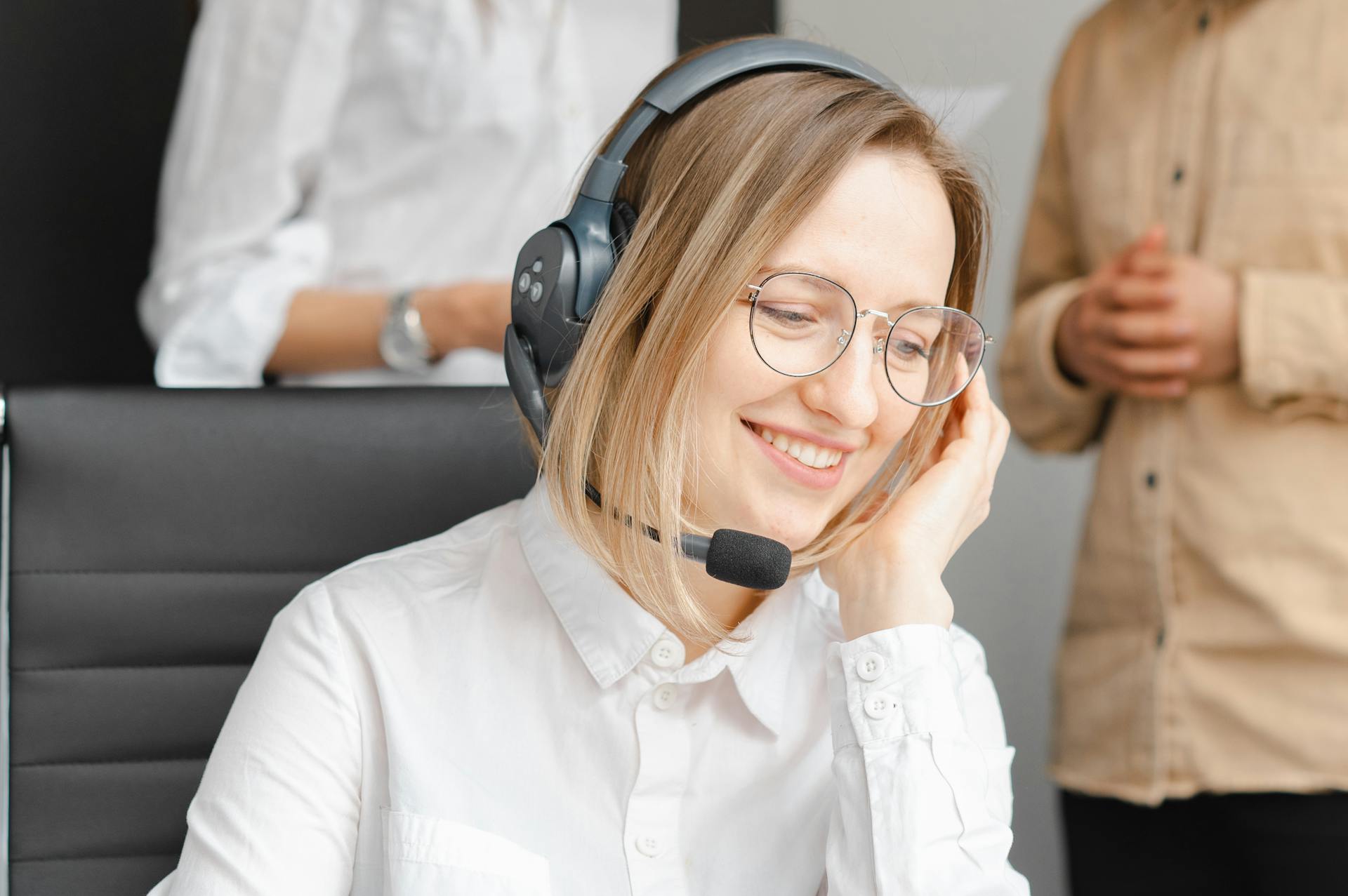 A woman with glasses and headphones smiling as she talks into the microphone.